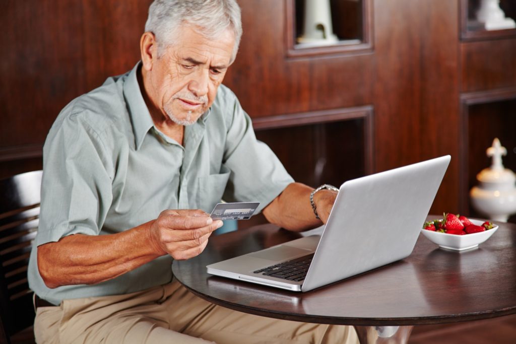 senior man at laptop paying with credit card for online shopping