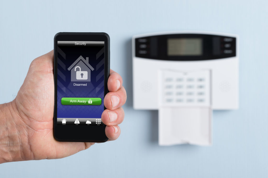 close-up of a person's hand holding remote control of security system. photographer owns copyright for images on screen
