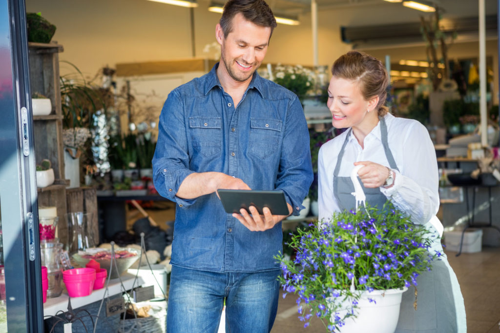 male customer using digital tablet while standing by florist holding potted plant in shop