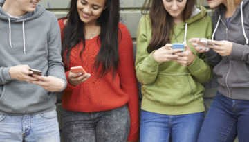 Group Of Teenagers Sharing Text Message On Mobile Phones